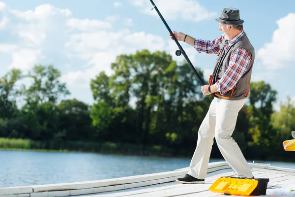 Bearded grey-haired man pulling fishing tackle while fishing — Stock Photo, Image