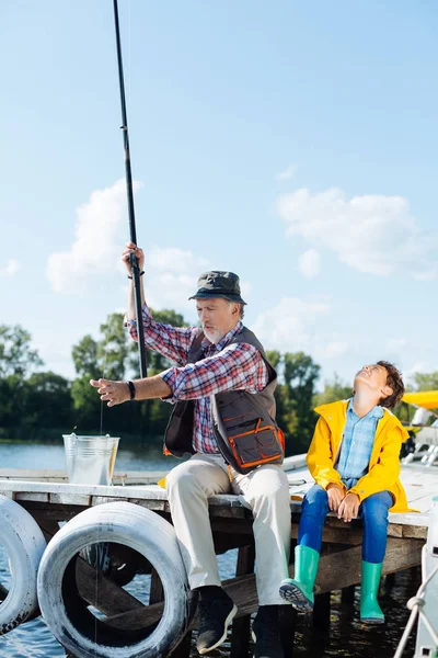 Pensionato dai capelli grigi tirando attrezzatura da pesca durante la cattura del pesce — Foto Stock