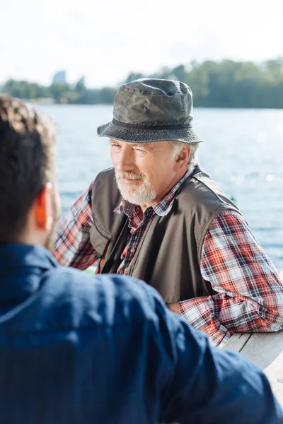 胡子退休男子说话与儿子，而坐在湖边 — 图库照片