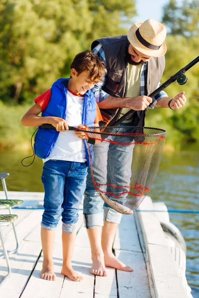 Figlio guardando in rete da pesca dopo la cattura di pesce con il padre — Foto Stock