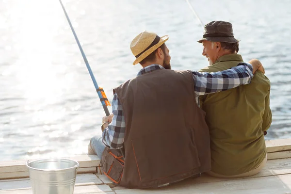 Skäggiga mannen kramar sin pensionerade far samtidigt som de fiskar tillsammans — Stockfoto