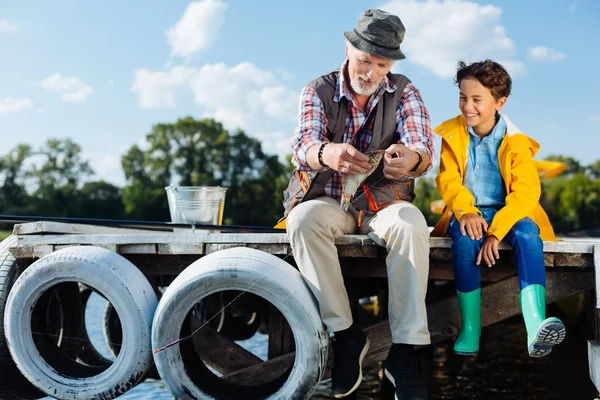 Nieto sonriendo mientras mira los peces capturados por el abuelo — Foto de Stock