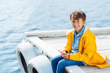 Neşeli koyu gözlü çocuk nehir kenarında otururken mutlu hissediyor