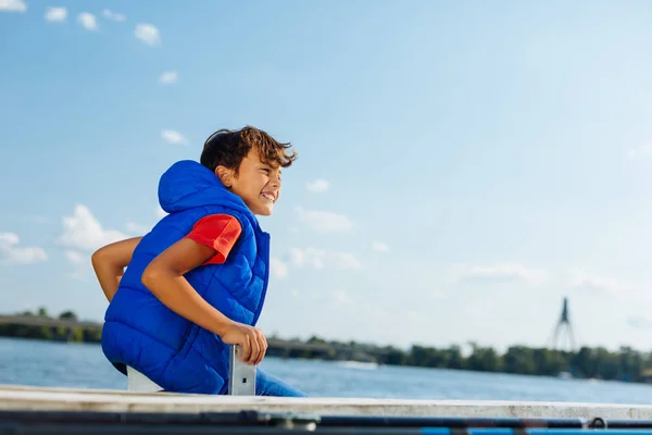 Ragazzo allegro seduto vicino al fiume e godersi la vista — Foto Stock