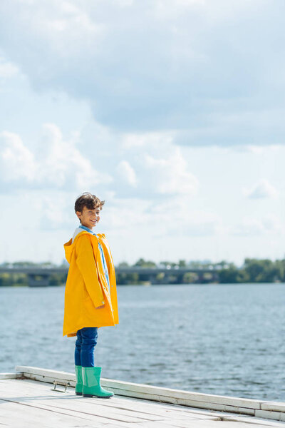 Handsome boy wearing bright rain boots standing near river