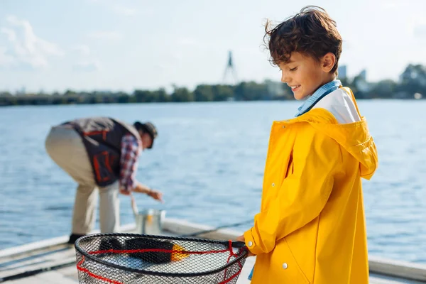 Niño sonriente usando impermeable amarillo sosteniendo red de pesca — Foto de Stock
