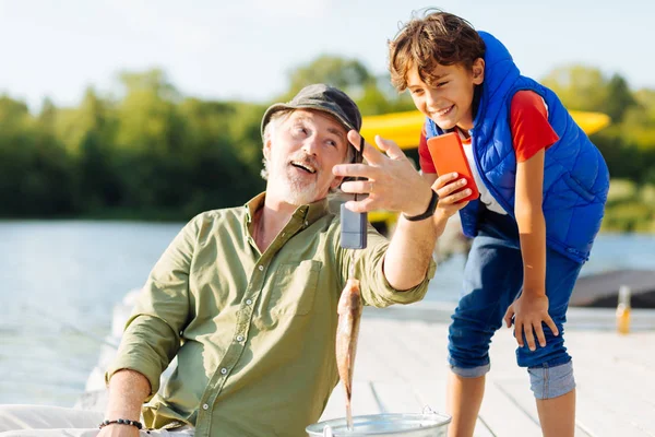 Menino fazendo foto de peixe grande enquanto pesca com o avô — Fotografia de Stock