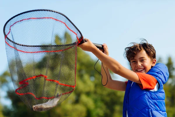 Beaming dark-haired boy holding fishing net with fish — Stock Photo, Image