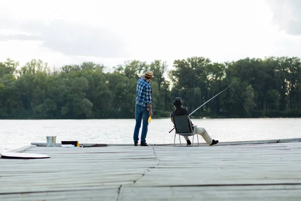 男人戴帽子说话的父亲坐在和捕鱼 — 图库照片