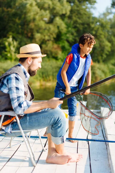 Menino de cabelos escuros segurando rede enquanto a pesca com o pai — Fotografia de Stock