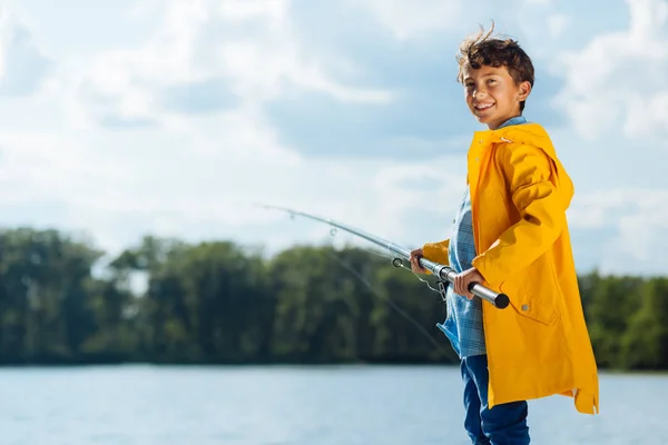 Menino vestindo capa de chuva amarela sorrindo enquanto pesca — Fotografia de Stock
