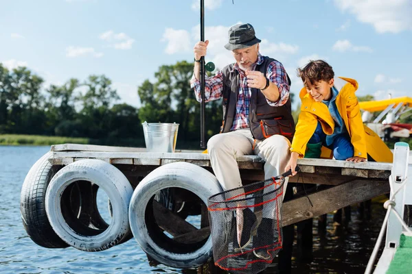 Niño poniendo la red en el agua mientras pesca con el abuelo — Foto de Stock