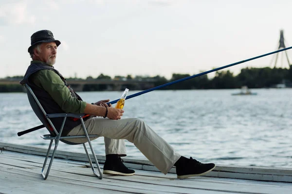 养老金领取者在钓鱼时用一瓶啤酒冷却 — 图库照片