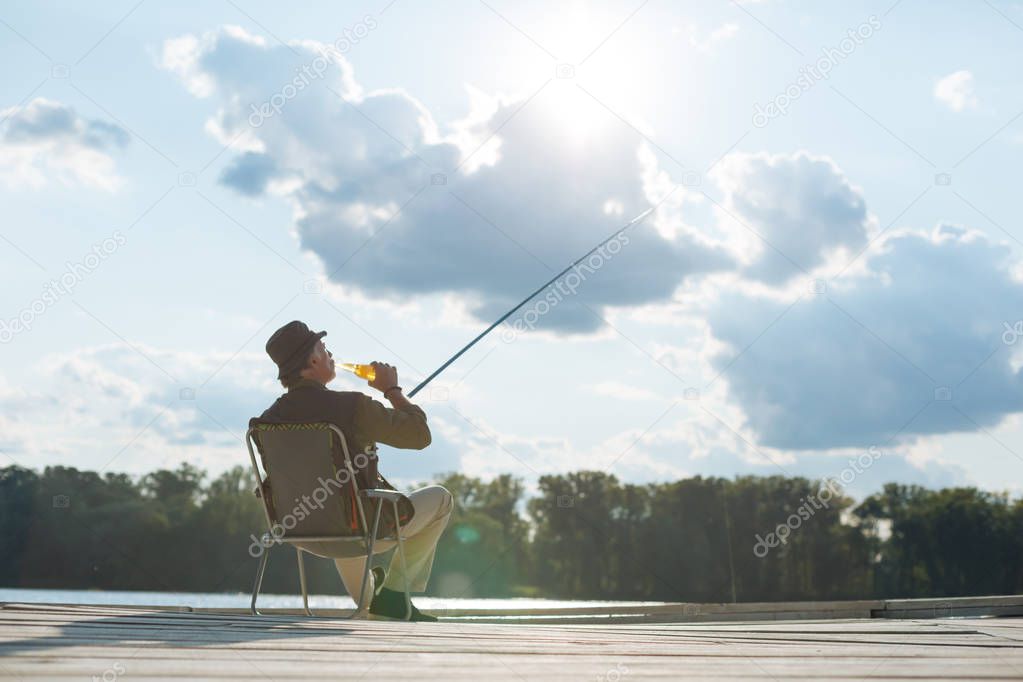 Retired man drinking beer and fishing in summer