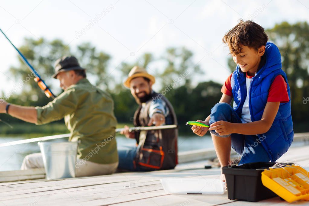 Helpful son smiling while giving fishing hook to father