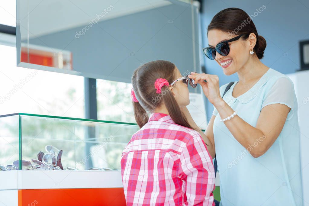 Pleasant brunette woman helping her daughter with eyeglasses