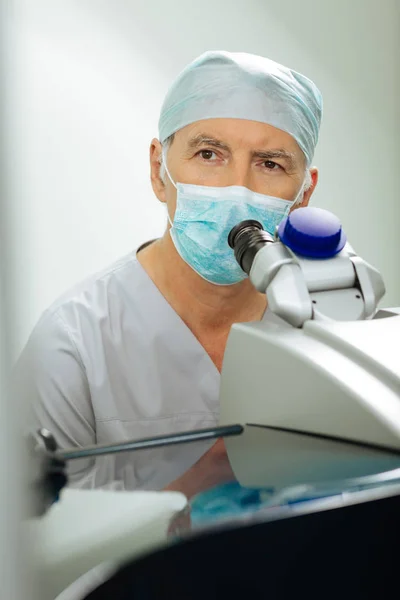 Inteligente optometrista masculino sentado ao microscópio — Fotografia de Stock