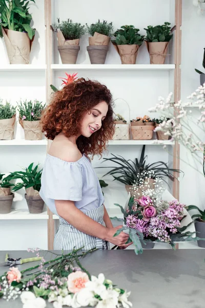Red-haired smiling professional florist ending composing bouquet