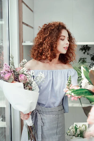 Meraklı görünümlü kırmızı saçlı kadın stokta farklı çiçekler bakıyor