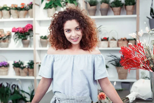 Çiçekçide açık üniforma giyen büyük mavi gözlü kararlı kırmızı saçlı kız