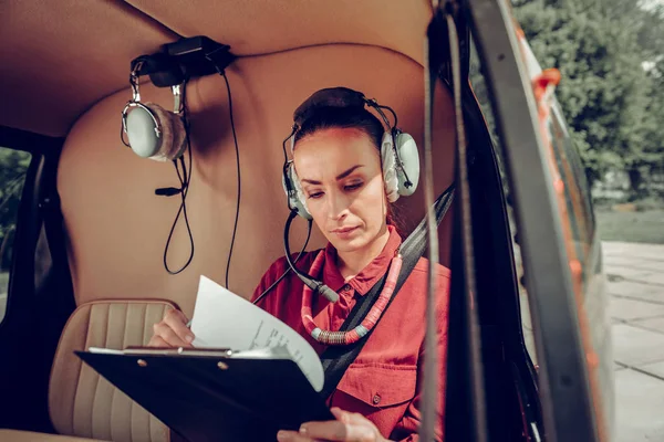 Female pilot wearing red shirt checking the documents in the helicopter