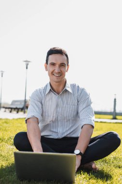 Bilgisayarıyla çimlerin üzerinde oturan adam