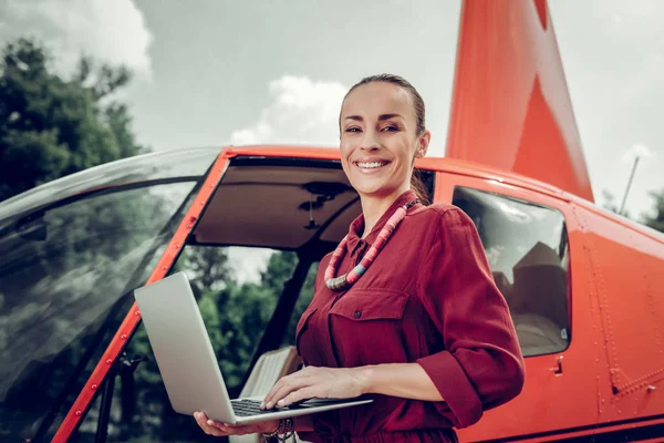 Beaming businesswoman writing e-mail standing near helicopter