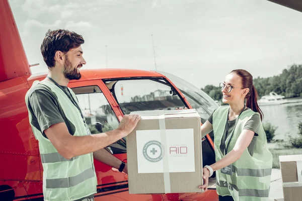 Vousatý humanitární pracovník pomáhající svému kolegovi v držení těžké skříňky — Stock fotografie