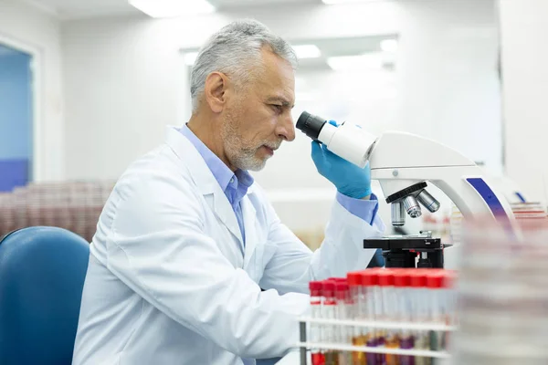 Persona masculina madura grave mirando al microscopio — Foto de Stock