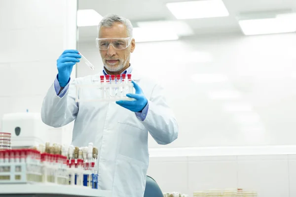 Delighted grey-haired man staring at test tube — Stock Photo, Image
