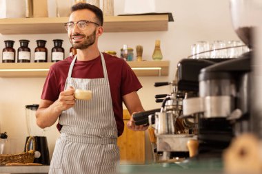 Neşeli barista kahve makinesi yanında kahve fincanı ile ayakta