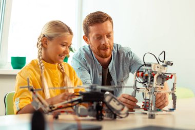 Gülümseyen kız öğretmeni bir robot bina bakıyor.