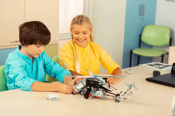 Fröhliches Mädchen schaut ihren Mitschüler beim Bau eines Hubschraubers an — Stockfoto