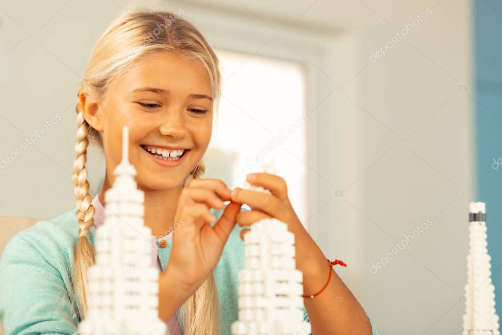 Cheerful schoolgirl looking at details while building.