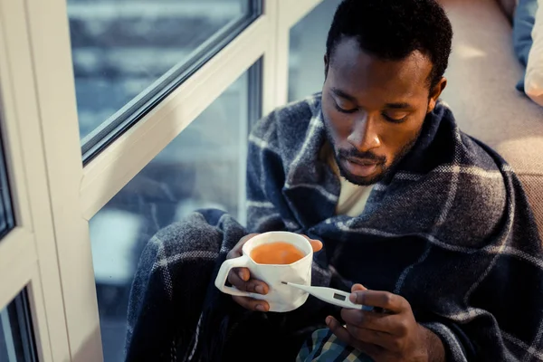 Ernstige, donker gevilde man die zijn lichaamstemperatuur meet — Stockfoto