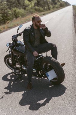 Motosikletin üstünde sigara içerek poz veren seksi vahşi motorcu.