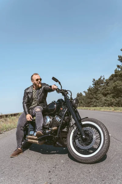 Красивый бородатый парень позирует на мотоцикле, глядя в сторону. — стоковое фото