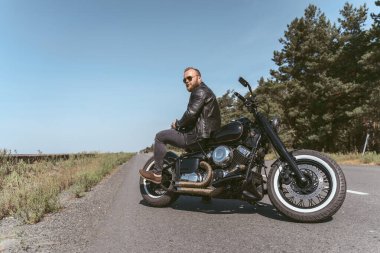 Yakışıklı sakallı adam bisikletin arkasında oturmuş poz veriyor.