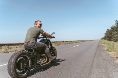 Bisiklet süren kaslı bir motorcunun arka görüntüsü.