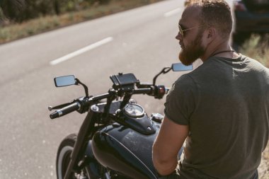 Motosikletinde oturan sakallı bir motorcunun arka görüntüsü.