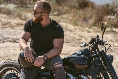 Motosikletli seksi sakallı bisikletçi poz verirken oturuyor.