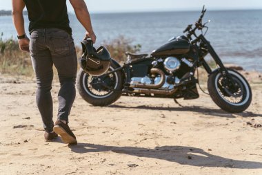 Motosikletine doğru yürüyen formda bir motorcunun arka görüntüsü.