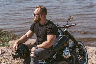 Bisikletinde kaskı olan ciddi görünümlü sakallı bir motorcu.