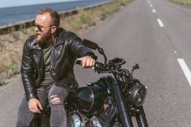 Deri ceketli yakışıklı sporcu yolda bisikletinin üstünde oturuyor.