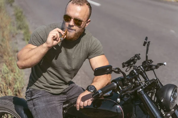 Уверенный бородатый байкер с сигаром, позирующий на велосипеде — стоковое фото