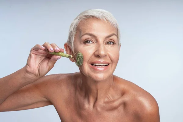 Sorridente signora felice utilizzando rullo di giada sul suo viso — Foto Stock