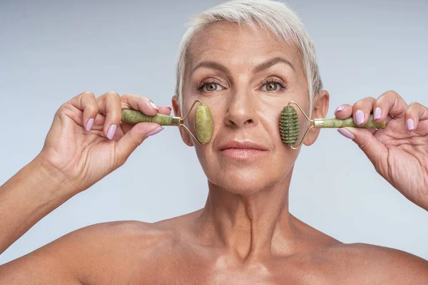 Mooi oud wijfje met twee beauty rollers in haar gezicht — Stockfoto