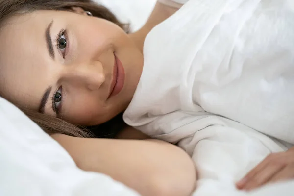 Улыбающаяся юная кавказка лежит в постели — стоковое фото