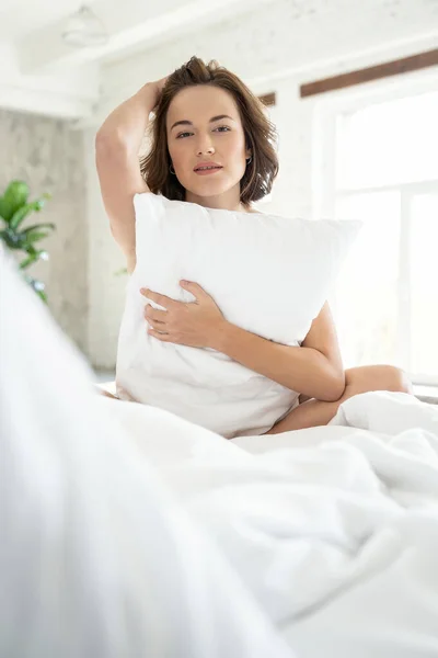 Mujer tranquila sosteniendo una almohada en la cama —  Fotos de Stock