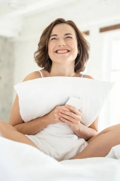 Mujer con un smartphone sentado en la cama — Foto de Stock